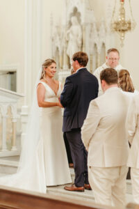 Bride and groom exchange vows at a church altar, surrounded by their wedding party and clergy during the ceremony.