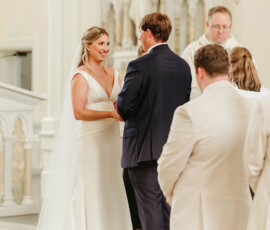 Bride and groom exchange vows at a church altar, surrounded by their wedding party and clergy during the ceremony.