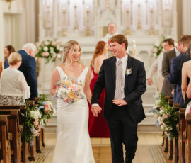 Smiling bride and groom walk hand in hand down the church aisle after their Louisiana wedding, surrounded by guests.