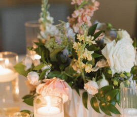 Elegant floral centerpiece with white and blush flowers, greenery, and votive candles on a light tablecloth for New Orleans weddings.