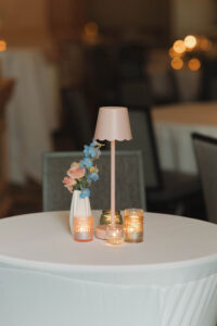 Elegant round table with white cloth, pink lamp, pastel flowers, and lit candles—ideal for a New Orleans wedding.