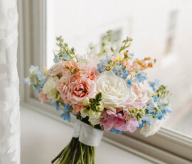Pastel bouquet with white, pink, and blue flowers wrapped in ribbon on a bright windowsill, ideal for New Orleans weddings.