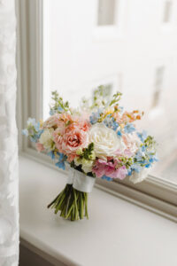 Pastel bouquet with white, pink, and blue flowers wrapped in ribbon on a bright windowsill, ideal for New Orleans weddings.