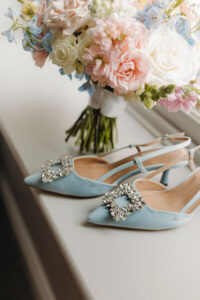 Light blue jeweled heels in front of a pink, white, and blue bouquet on a windowsill—chic Gulf South wedding inspiration.