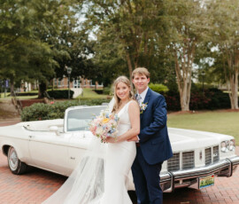Bride and groom smile by a white convertible on a brick path, celebrating their elegant New Orleans wedding outdoors.