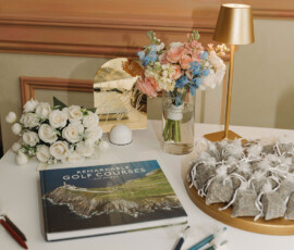 Wedding inspiration: table with roses, flower arrangement, “Remarkable Golf Courses” book, gold lamp, and elegant gold sign.