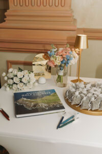 Wedding inspiration: table with roses, flower arrangement, “Remarkable Golf Courses” book, gold lamp, and elegant gold sign.