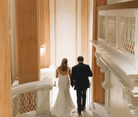 Bride and groom descend marble stairs in a grand, warmly lit hall with gold accents at a New Orleans wedding.