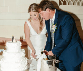 Bride in white dress and groom in blue suit cut wedding cake at a candle-lit table, classic New Orleans style.