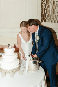 Bride in white dress and groom in blue suit cut wedding cake at a candle-lit table, classic New Orleans style.