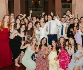 Formal wedding guests pose indoors with drinks, making playful claw gestures and smiling at a joyful Gulf South celebration.