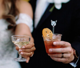 Bride with champagne and groom with cocktail toast at their Gulf South wedding, yellow flowers softly blurred in the background.
