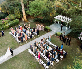 Bride and groom at altar in elegant New Orleans wedding, guests seated, attendants nearby, lush greenery and flowers.