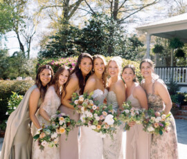 Bride in white with bridesmaids in pastel dresses smile outdoors, holding bouquets amid sunlit greenery and Southern wedding charm.