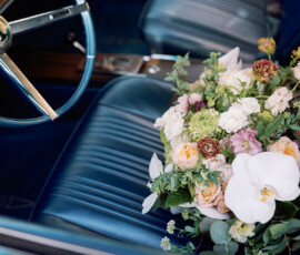 Bouquet of roses and orchids on a blue leather classic car seat, steering wheel visible—romantic Louisiana wedding inspiration.