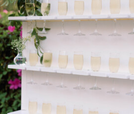 Champagne glasses with bubbly drinks on white shelves, accented by greenery and flowers for a chic New Orleans wedding.