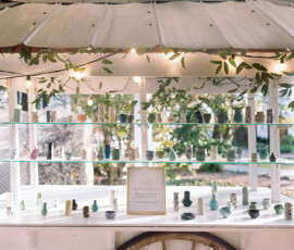 White cart with ceramic vases, greenery above, a framed sign, string lights, and garden backdrop at Louisiana wedding.