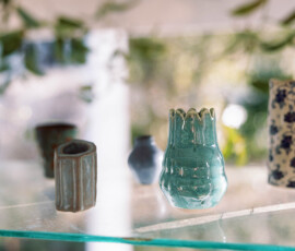 Small ceramic vases in assorted shapes, colors, and patterns on a glass shelf with greenery—stylish Louisiana wedding decor.