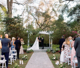 Bride and groom exchange vows at an outdoor altar, trees and guests creating a romantic New Orleans wedding scene.