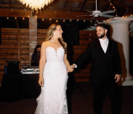 Bride and groom hold hands and smile while dancing under a chandelier at their New Orleans wedding reception.