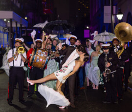 A couple dances and kisses at night in the street, amid a brass band and joyful crowd at a vibrant New Orleans wedding.