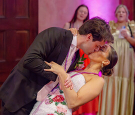A man in a suit dips and kisses a woman in a beaded dress at a romantic Louisiana wedding as guests look on.