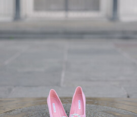 Pink high heels with jeweled bows on an ornate surface outdoors, ideal for wedding inspiration, gate and steps blurred behind.