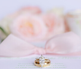 Gold marquise diamond ring on wedding invitation with pink bow and soft floral background, evoking New Orleans elegance.