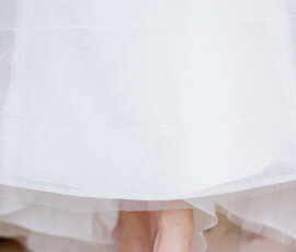 Person in a white dress with pink flower detail and jeweled pink heels stands on a light floor at a Louisiana wedding.