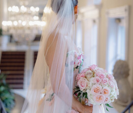 Bride in white dress and veil with pink and white roses, by a staircase at her elegant New Orleans wedding.