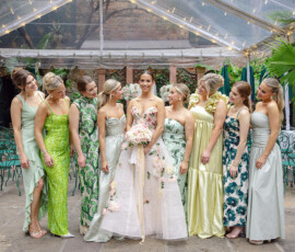 Bride in floral gown with bouquet smiling alongside bridesmaids in green dresses under a string-lit tent at Gulf South wedding.