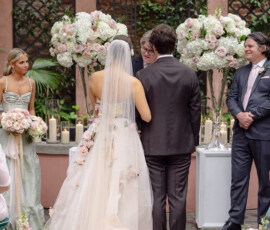 Bride in floral dress and veil with groom at outdoor Louisiana wedding, surrounded by bridal party, flowers, and candles.