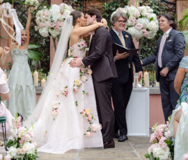 Bride in floral gown and veil kisses groom at Louisiana wedding as smiling guests celebrate amid vibrant flowers.