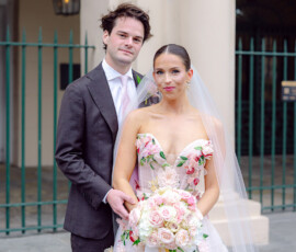 Bride in floral dress with rose bouquet stands by groom in dark suit outdoors, evoking classic Louisiana wedding style.