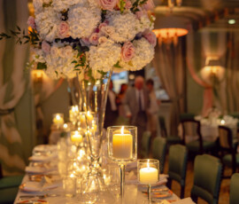Elegant dinner table with tall white and pink floral centerpieces, candles, and place settings in a warm Louisiana wedding venue.
