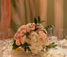 Elegant pink and white rose centerpiece with greenery on a table, wine glasses, candle, and water at a Louisiana wedding.