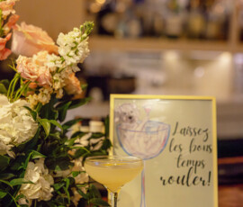 Cocktail on wooden bar with flowers and “Laissez les bons temps rouler!” sign in cozy, warm Gulf South wedding setting.