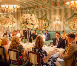 Elegantly dressed people dine in a lavish, green-themed restaurant with chandeliers and flowers, evoking a festive Louisiana wedding.