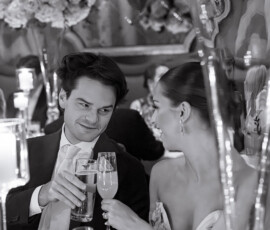 A formally dressed couple toasts with champagne at an elegant Louisiana wedding, surrounded by flowers and candlelight.