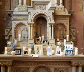Memorial table with framed family photos, candles, and white and blue florals arranged on an ornate church altar.