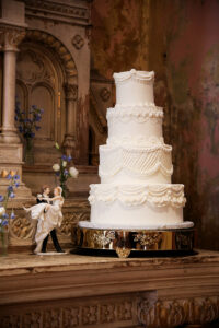 Classic tiered white wedding cake with ornate piping details and a bride and groom cake topper, displayed on an elegant stand.