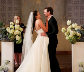 Bride and groom share a joyful moment during their ceremony, surrounded by white and blue floral arrangements at the altar.