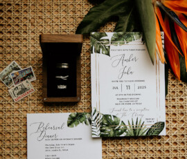 Tropical wedding invitation suite with green leaves, RSVP card, LA postcards, rings in a box, and bird of paradise flower.