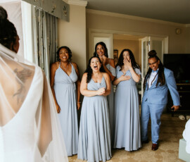Bride with bridesmaids in light blue dresses and a groomsman in a hotel room, smiling before Louisiana wedding.