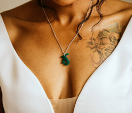 Woman in white v-neck dress with lion tattoo on shoulder and green number 5 pendant, Gulf South wedding inspiration.