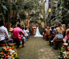 Bride and groom at an outdoor altar with string lights, trees, and flower-decorated benches—Louisiana wedding inspiration.