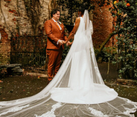 Bride and groom hold hands outside, surrounded by greenery, brick walls, and vibrant flowers at their New Orleans wedding.