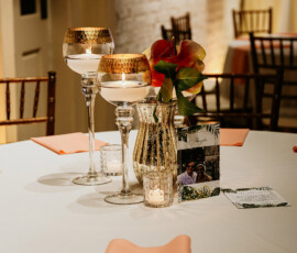 Elegant Gulf South wedding table: peach napkins, gold vase with red-orange flowers, candles, and a small photo centerpiece.