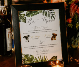 Tropical bar menu in elegant script with candles, bottles, and flowers, capturing a lively Louisiana wedding vibe.