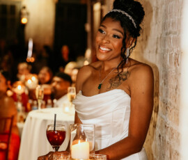 Bride in a white dress smiling by a candlelit table at a cozy indoor New Orleans wedding reception.